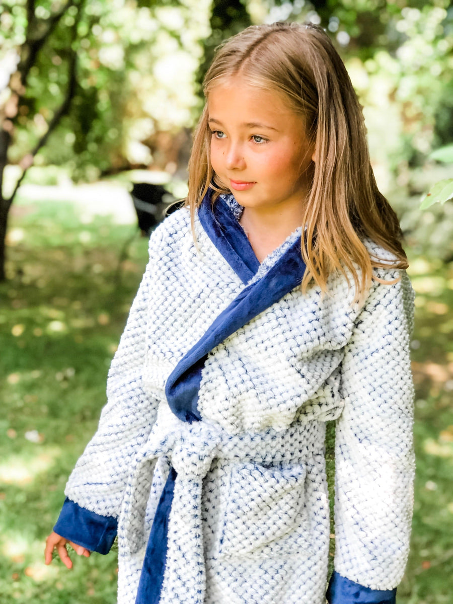 A female child wearing a white fluffy doted robe with a blue background and blue edged children's robe.