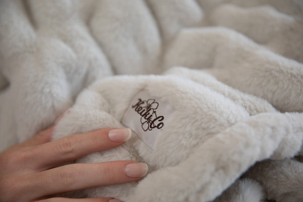 A hand resting on cream faux fur with the Keiki Co. logo embroidered into the pile