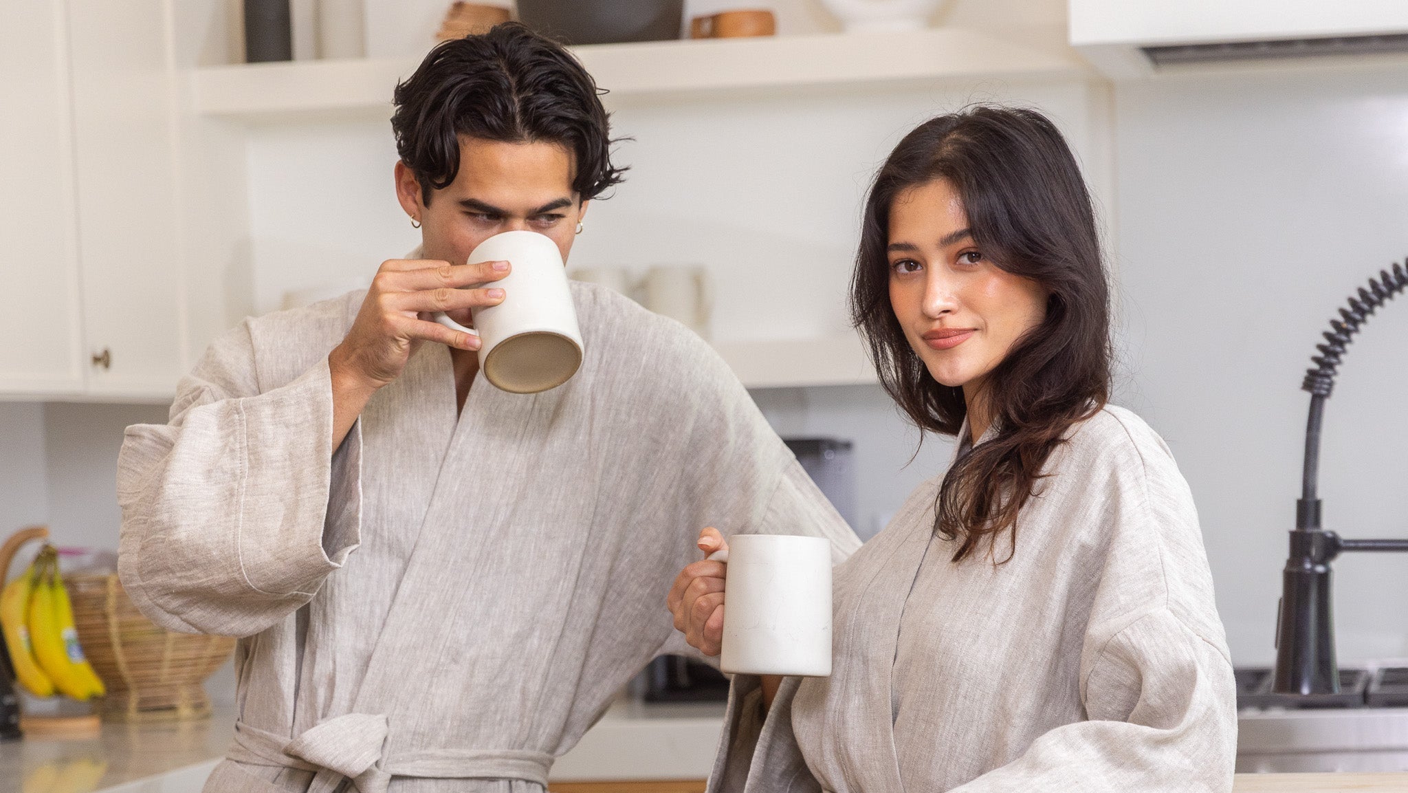 A couple touching glasses in kitchen wearing matching robes