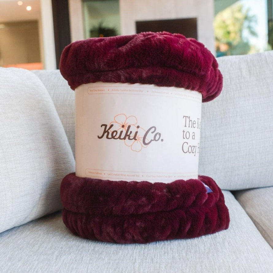 Bordeaux Cloud Throw, a burgundy color in gift packaging ready to ship, on couch.