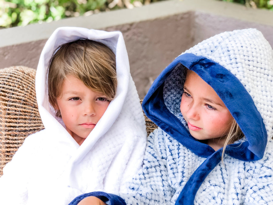 A female child wearing a white fluffy doted robe with a blue background and blue edged children's robe with a male child wearing a white children's robe.