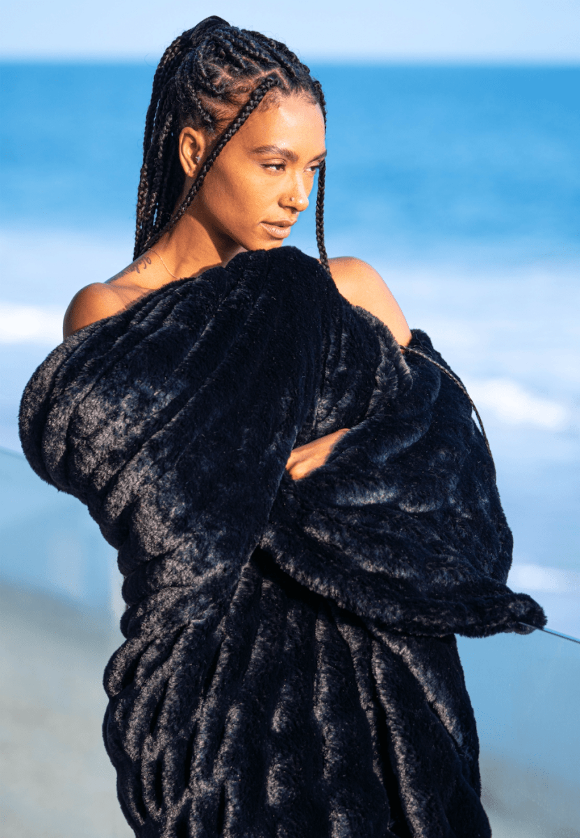 Caviar Black Cloud Throw ultra soft luxury faux fur weighted blanket wrapped around woman in luxury home by beach.