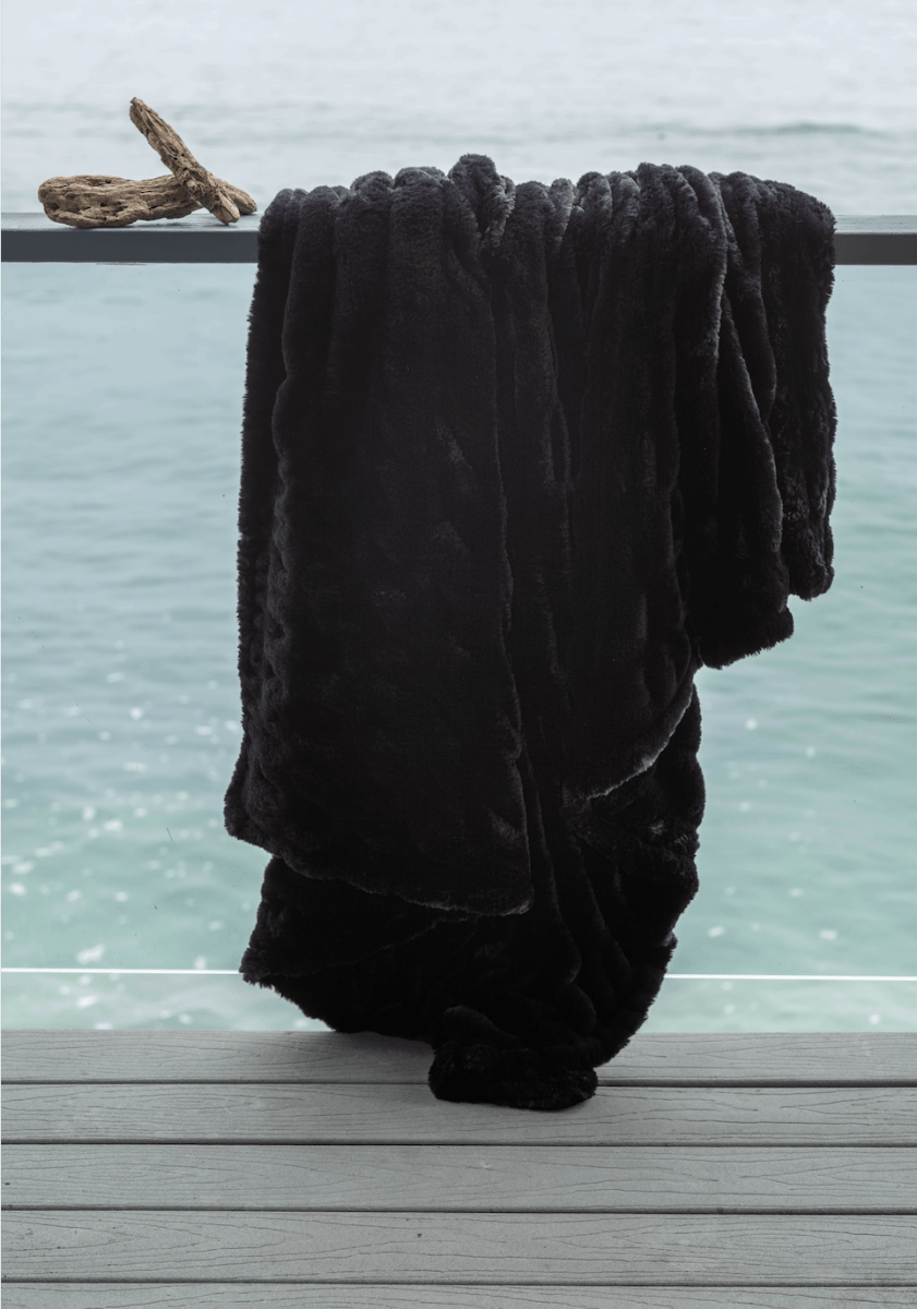 Caviar Black Cloud Throw ultra soft luxury faux fur weighted blanket draped in luxury home by beach.